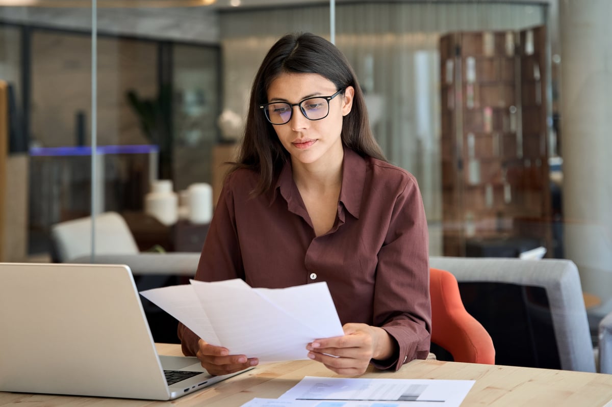 A professional reviewing financial reports and market data at her desk