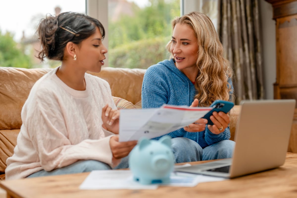 Two friends reviewing financial documents together while discussing budgeting and saving